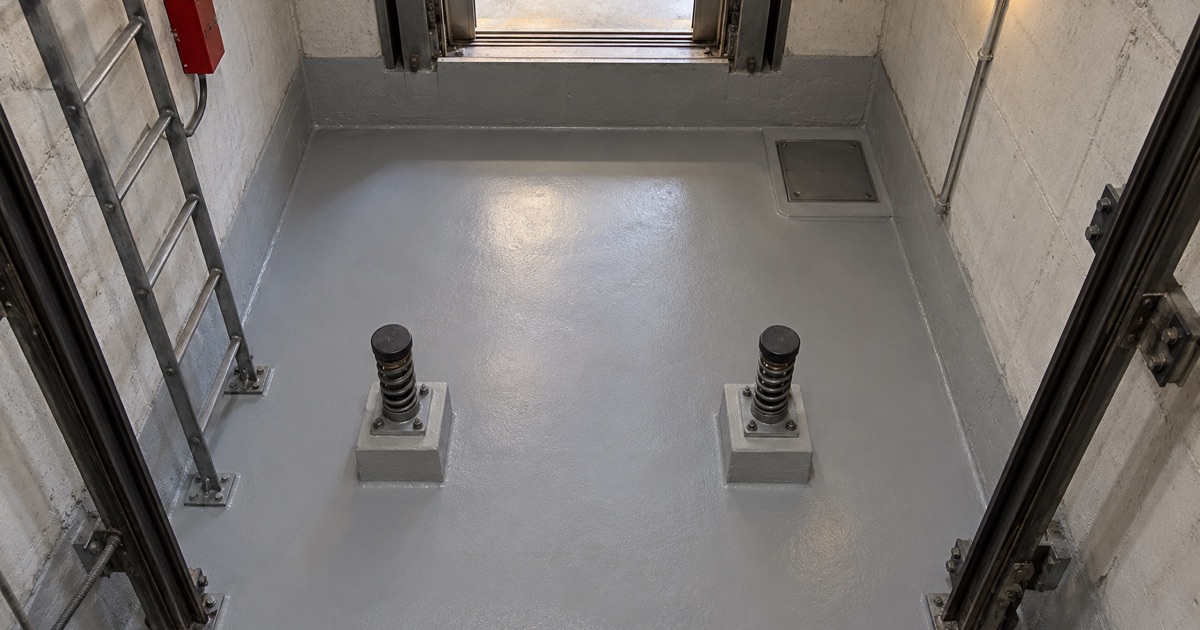 A coated elevator pit floor in a Westchester office building, finished around the buffers, the pit ladder and the stop switch.